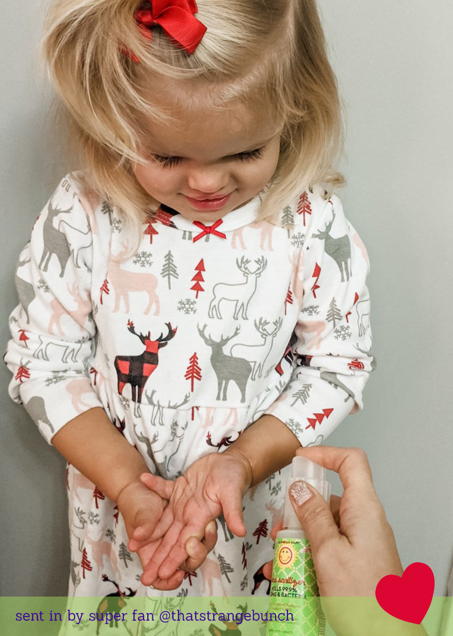 Child wearing a patterned shirt with animals and trees, parent is using California Baby hand sanitizer to clean hands